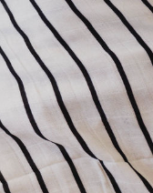Close-up of a Muslin Quilt | Black & White Yin Yang / Stripe, from the brand forever french baby, showcasing white fabric with evenly spaced black vertical stripes. The texture appears soft and slightly crumpled, with the stripes creating a simple, classic pattern in 100% muslin cotton.