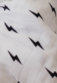 A close-up of the forever french baby Muslin Swaddle | Black & White Lightning Bolt, showcases an evenly spread pattern of small, black lightning bolts on the white fabric. The slightly wrinkled texture adds to its softness, making it perfect for baby comfort.