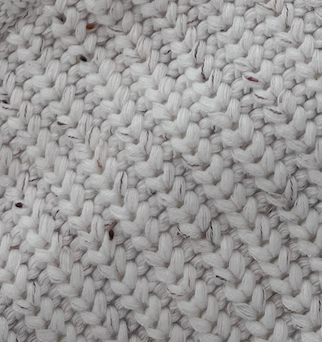 Close-up of a white hand-knitted Child Knit Sweater from forever french baby, featuring the Cloud Confetti design with intricate patterns and tight stitches. Subtle flecks of color add contrast to the soft, cozy texture.