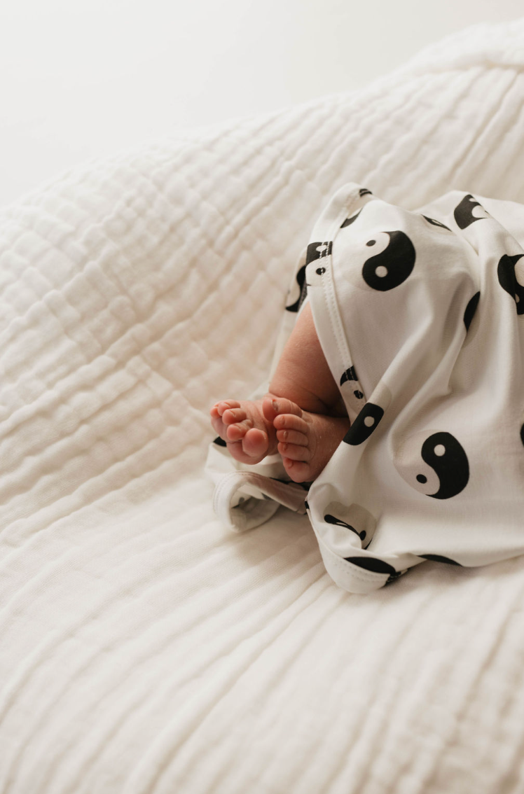 Close-up of a newborn baby's feet in white pajamas with a black and white yin-yang pattern, resting on the soft, quilted surface of the Bamboo Swaddle by forever french baby, made from hypo-allergenic, breathable fabric.