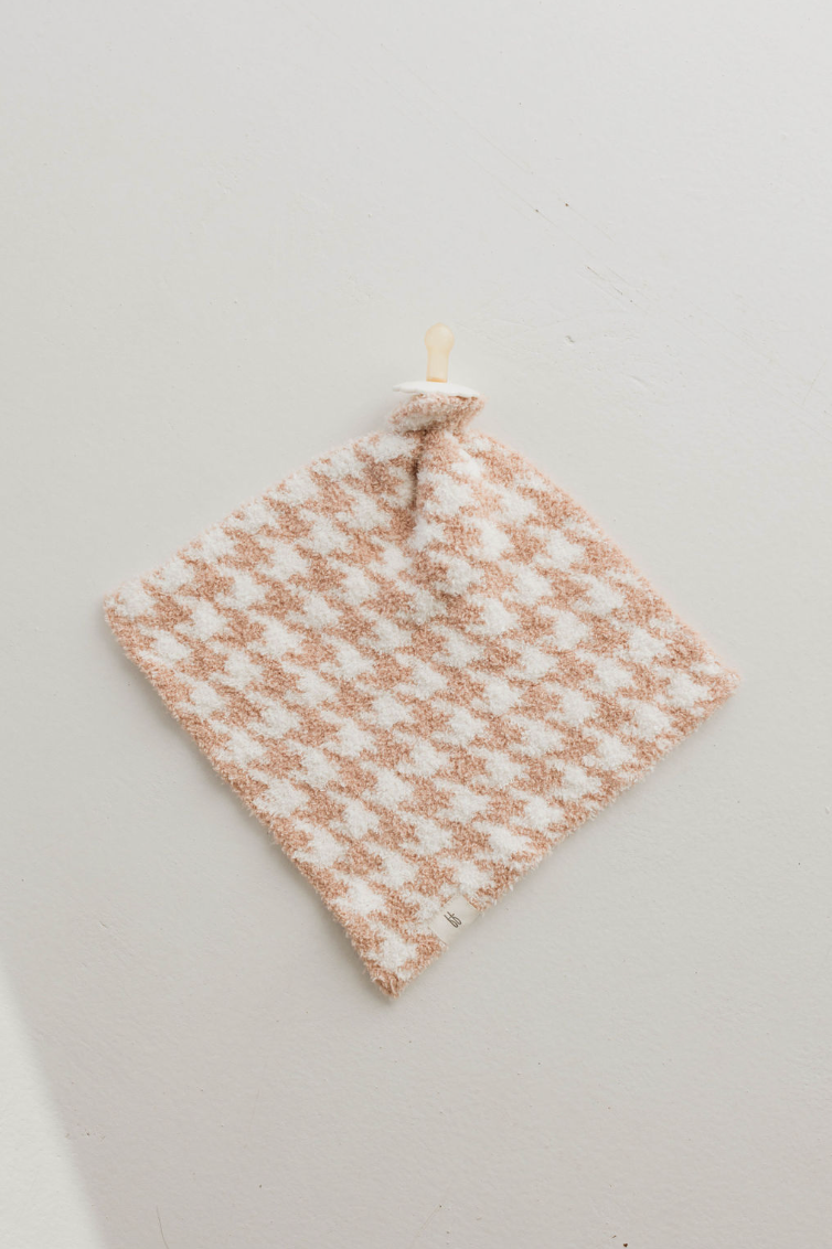 A Houndstooth Rosé and Cream Plush Lovey from forever french baby, featuring a charming beige and white checkerboard pattern complete with a beige pacifier attached at the top, lays flat on a light gray surface. The softest lovey for your little one, it appears incredibly plush and perfect for comfort.