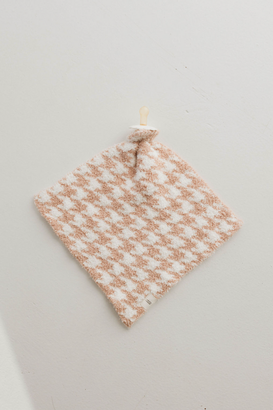 A Houndstooth Rosé and Cream Plush Lovey from forever french baby, featuring a charming beige and white checkerboard pattern complete with a beige pacifier attached at the top, lays flat on a light gray surface. The softest lovey for your little one, it appears incredibly plush and perfect for comfort.