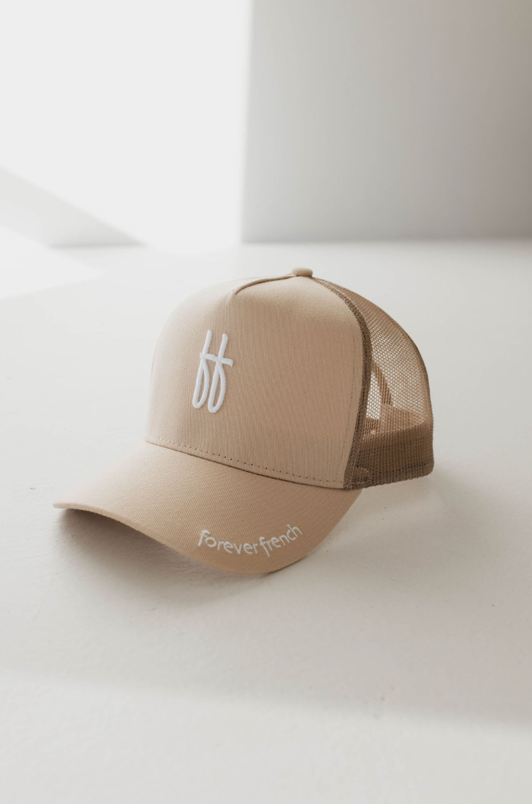 The Adult Trucker Hat | ff Tan by forever french baby features a beige mesh back and a front panel adorned with a white embroidered "ff" logo. Its curved brim showcases "forever french" embroidered in white. For maintenance, spot clean it with mild detergent as needed to keep your accessory looking fresh. The hat is displayed on a light-colored surface, casting a soft shadow at an angle from the light source.