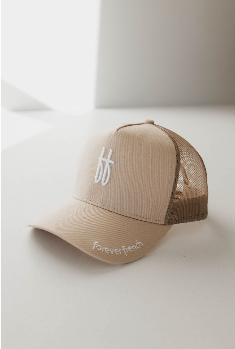 A tan Adult Trucker Hat from the brand forever french baby, featuring a mesh back and a white stitched logo with two intertwined lowercase 'f' letters on the front. The words "foreverfrench" are embroidered in white on the left side of the brim. Spot clean this accessory with mild detergent for best results.