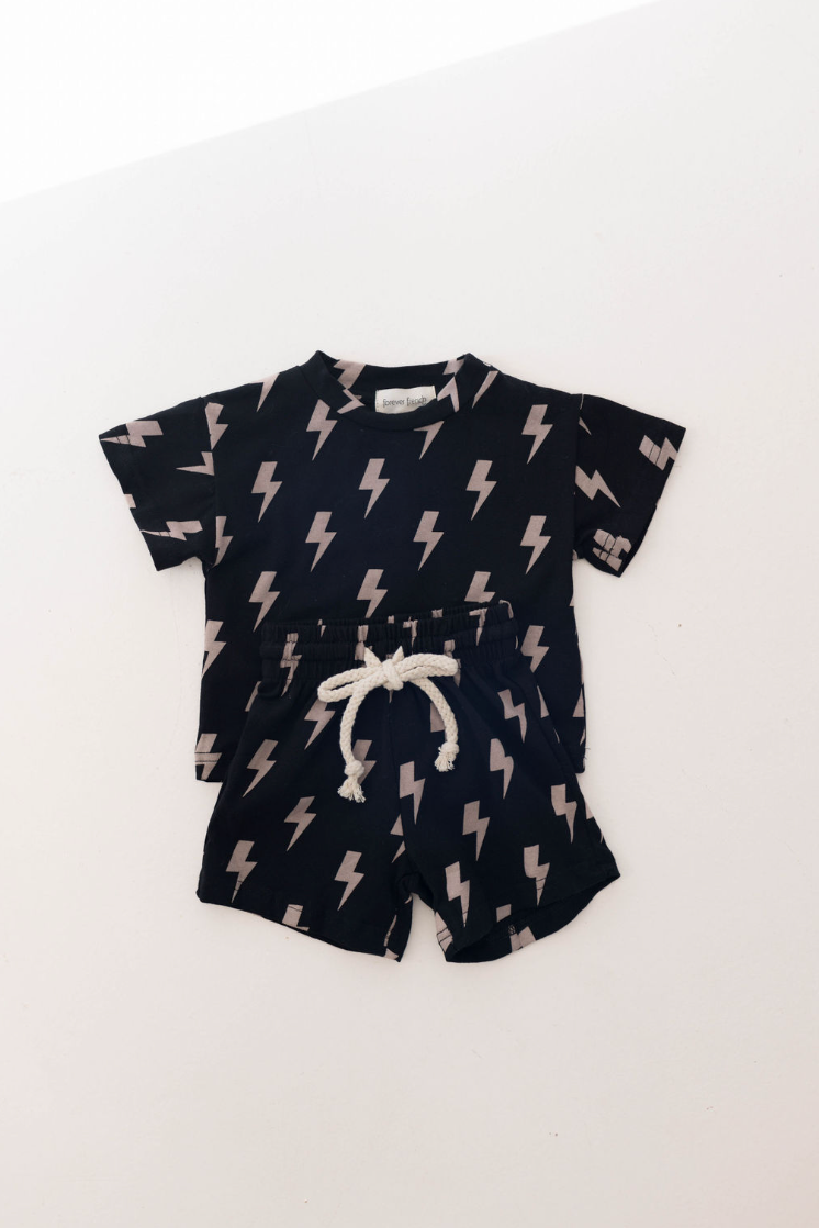 A child's 0-9 years Short Set | Black Lightning from forever french baby is perfect for summer. This outfit features a black short-sleeve t-shirt and shorts both adorned with white lightning bolts. The shorts also have a handy white drawstring at the waist.