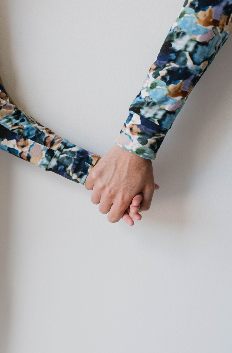 Two people holding hands, only their forearms and hands visible, both donning long-sleeve Women’s Bamboo Pajamas in the vibrant Charli Print from forever french baby. Their intertwined hands symbolize unity and affection against a plain white background.