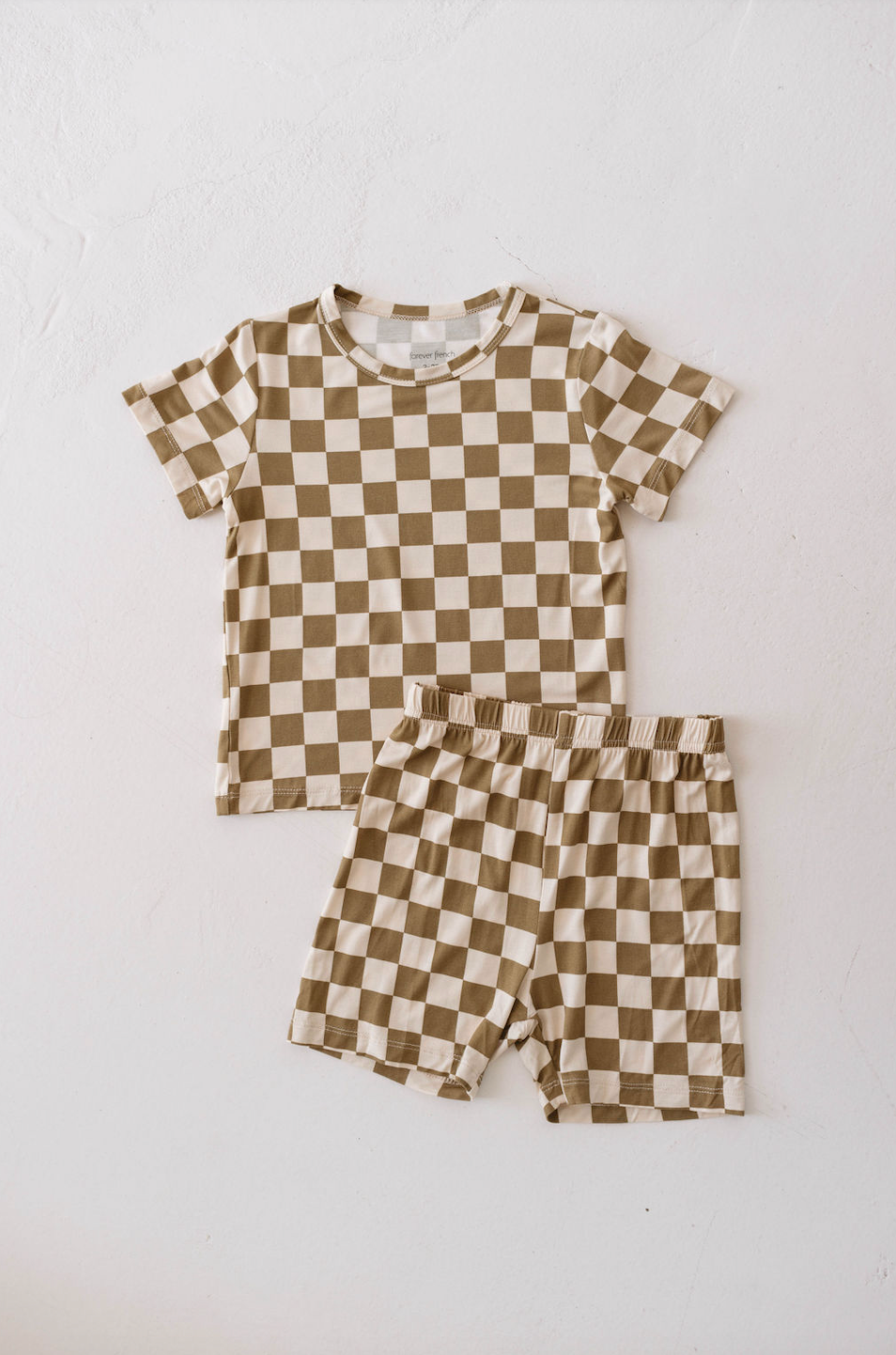 A matching set of children's clothing from forever french baby laid out on a white surface, consisting of a short-sleeved t-shirt and shorts. Both items feature an olive and white checkerboard pattern, crafted as breathable babywear for ultimate comfort—the Bamboo Short Set | Olive Checkerboard.