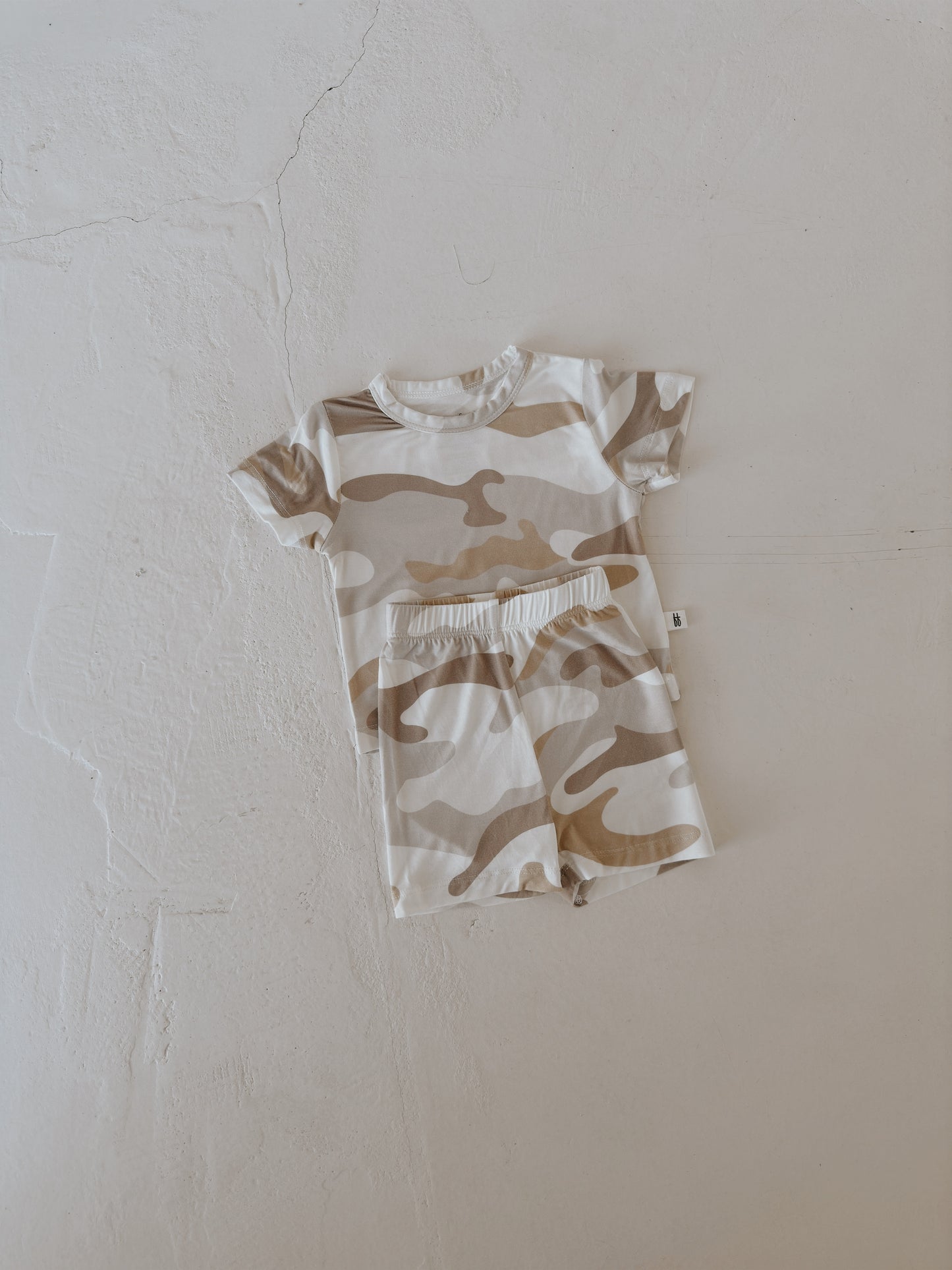 The Bamboo Short Set | Camo 2.0 by forever french baby is a beige and white, short-sleeve toddler romper with a camouflage pattern, made from breathable fabric and displayed flat on a light textured surface.
