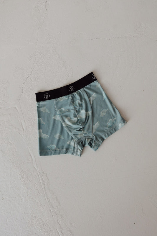 The Kendy 3 Toddler Bamboo Boxer Short | Duke features a light blue fabric with a white cloud pattern and black waistband, laid flat on a textured off-white surface. Made from breathable bamboo for comfort.