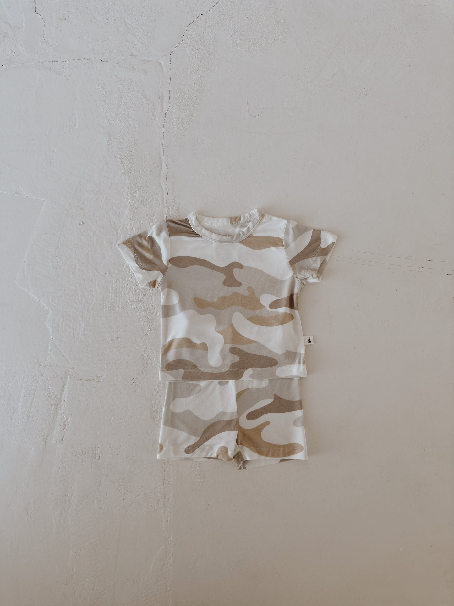 The forever french baby Bamboo Short Set | Camo 2.0 features a beige and white camo-patterned, short-sleeved top and shorts for toddlers, crafted from breathable fabric and displayed on a light textured surface.