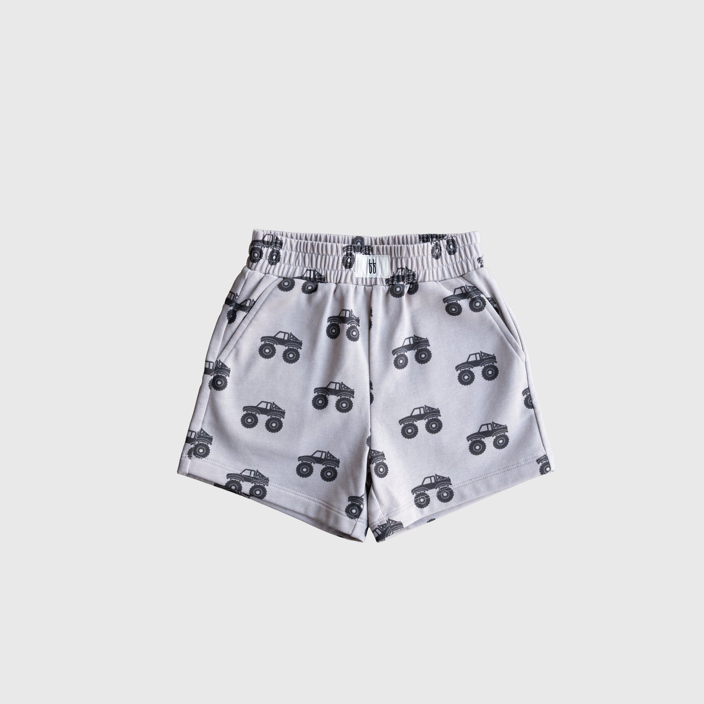 The French Terry Short Set | Monster Truck by forever french baby features light gray shorts with an elastic waistband, black monster trucks print, and side pockets. Pair with a short sleeve top for a stylish kids outfit. Shown on a plain white background.