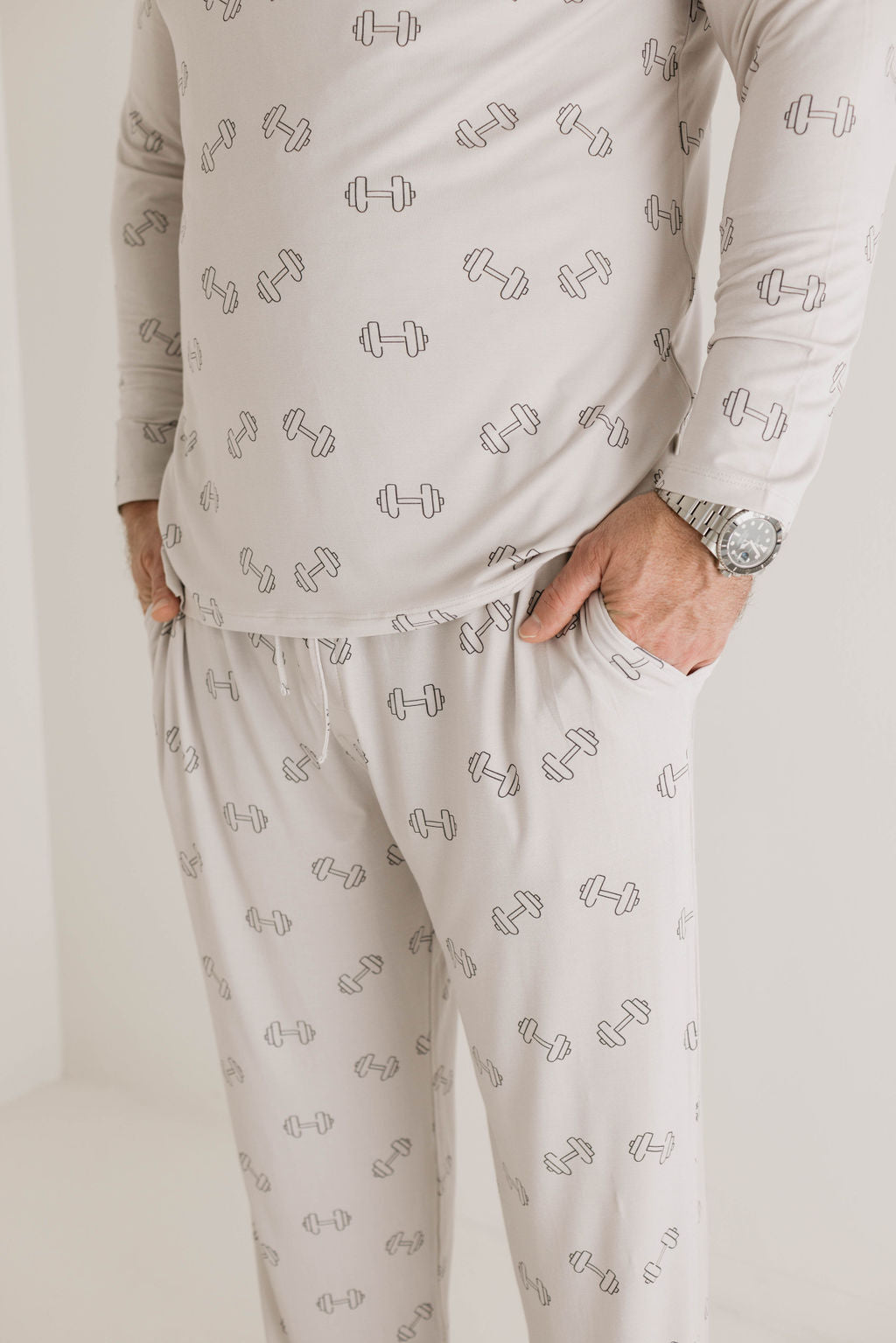 A person dressed in forever french baby's Adult Long Sleeve Bamboo Pajamas | Arm Day, showcasing a hand-drawn dumbbell weights graphic. They have one hand in their pocket and are wearing a wristwatch. The focus is on the torso and legs, ensuring a comfortable night's sleep, with no facial features visible.