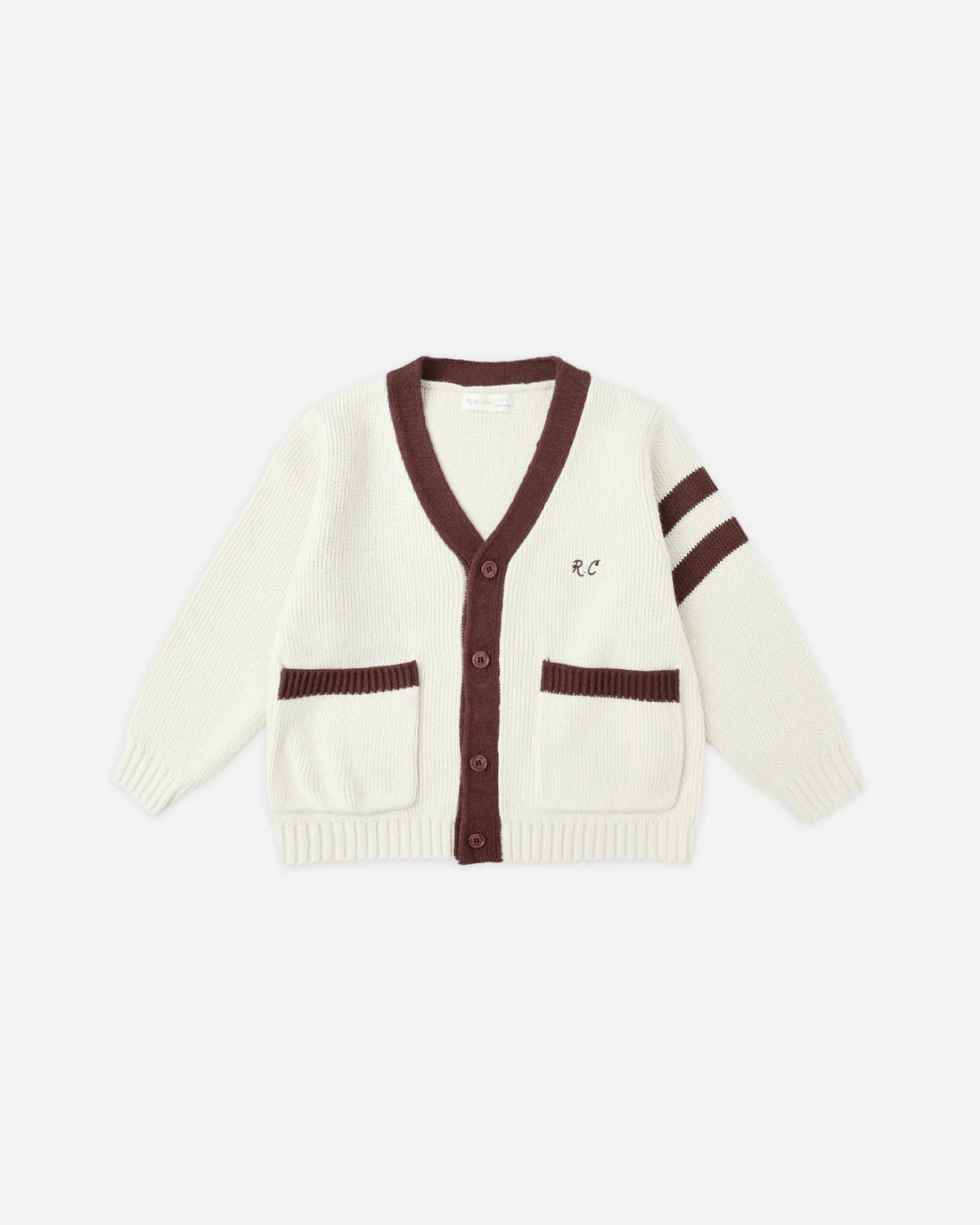 The Rylee + Cru Haywood Cardigan | Natural is a cream collegiate cardigan with brown contrast trim, two front pockets, and bold brown stripes on the left sleeve. An “R C” monogram decorates the left chest, and it is shown against a plain white background.