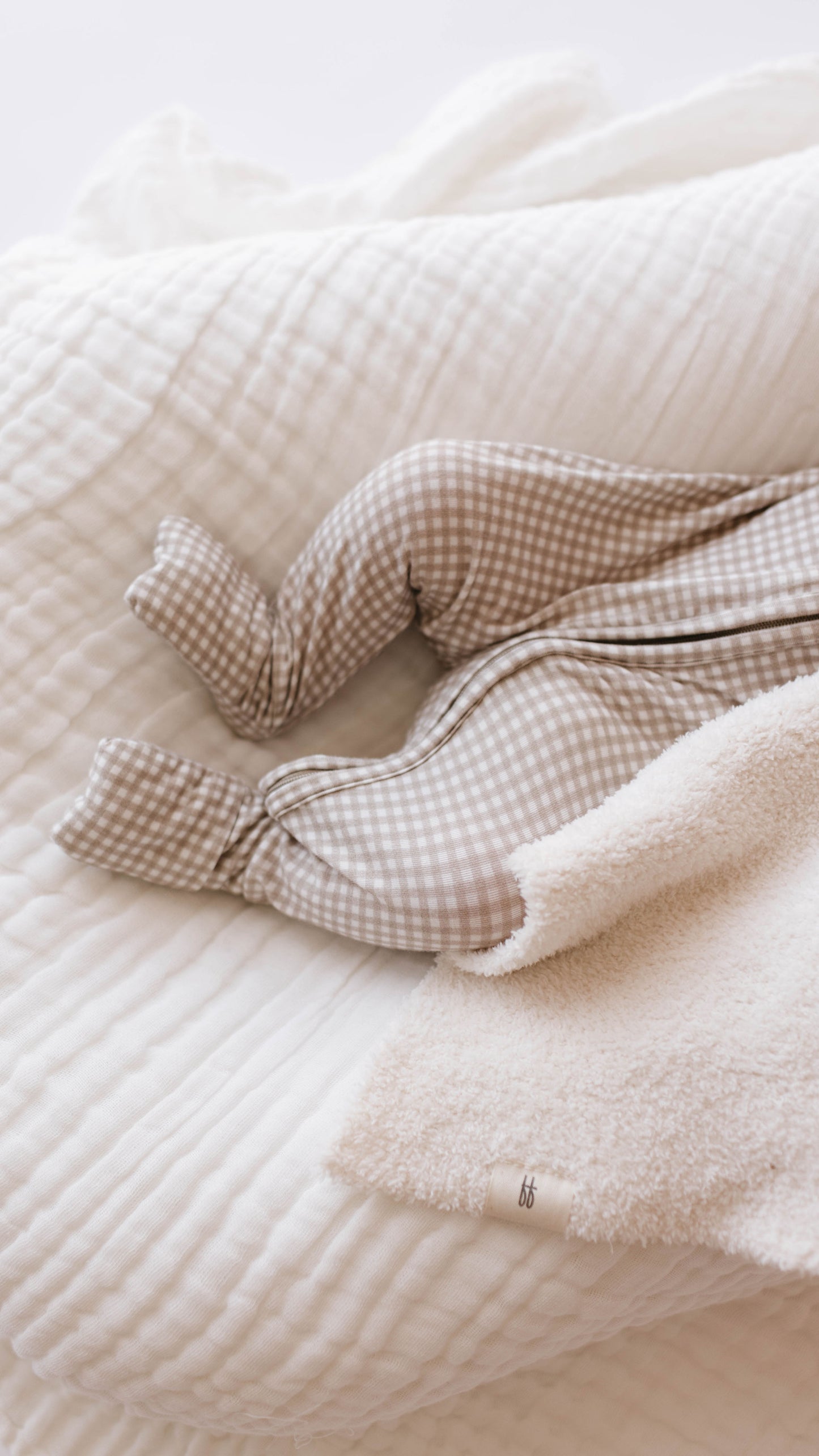 A baby wearing brown and white checkered pajamas lies on a Crib Sheet | Cloud by forever french baby. The baby's feet, enclosed in footed pajamas, are partially covered by a fluffy beige blanket. Only the lower legs and feet of this forever french baby are visible in the image.