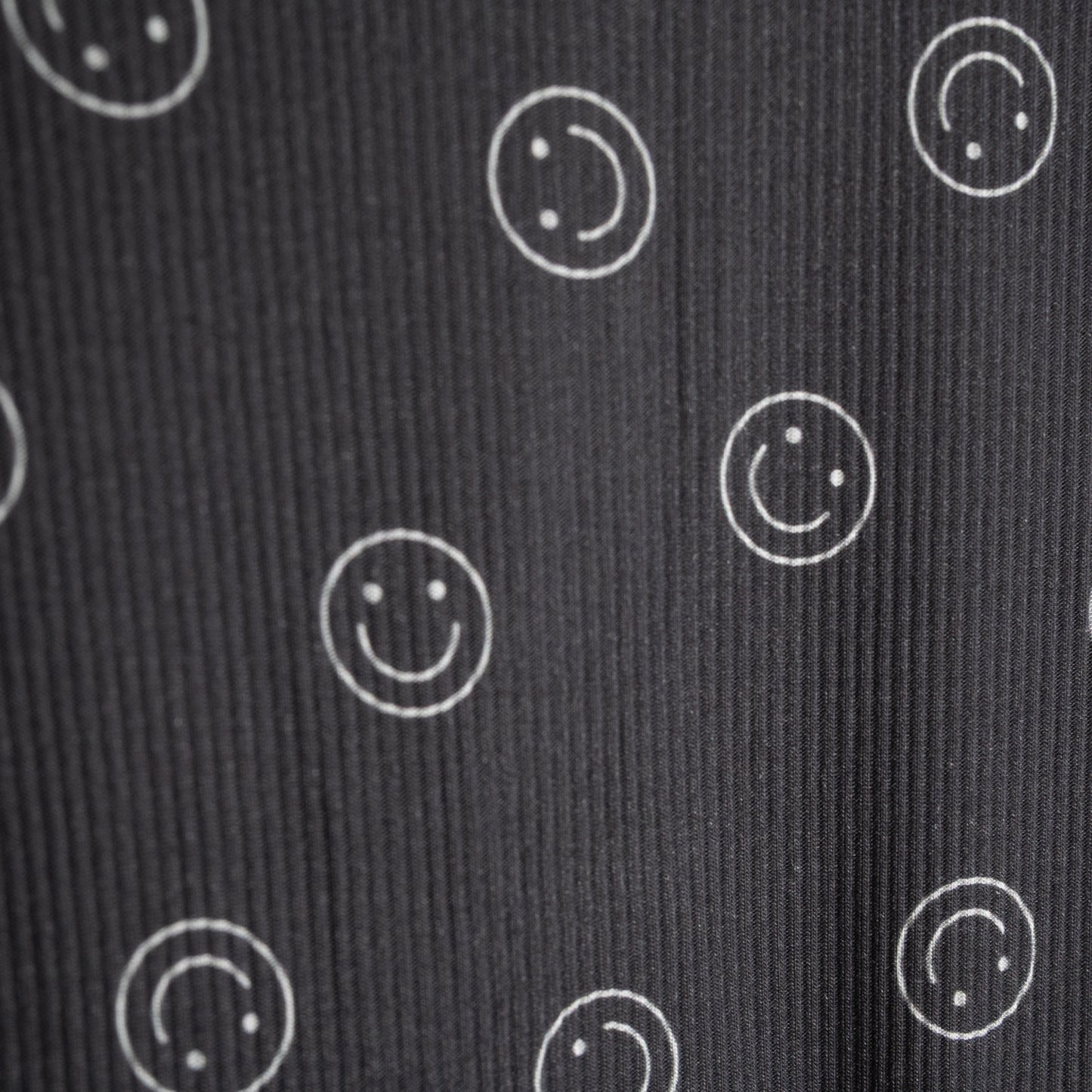 A close-up of the forever french baby Child Boxy Tee Lounge Set | Smiley Ribbed shows dark ribbed fabric with white outlined smiley faces, some full and some partial—perfectly spaced and ideal for comfy, breathable children's loungewear.