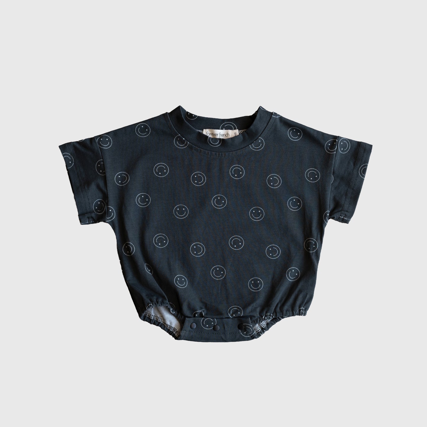 The forever french baby Short Sleeve Romper | Smiley features a dark gray cotton blend, light smiley face pattern, and short sleeves, shown laid flat on a white background.