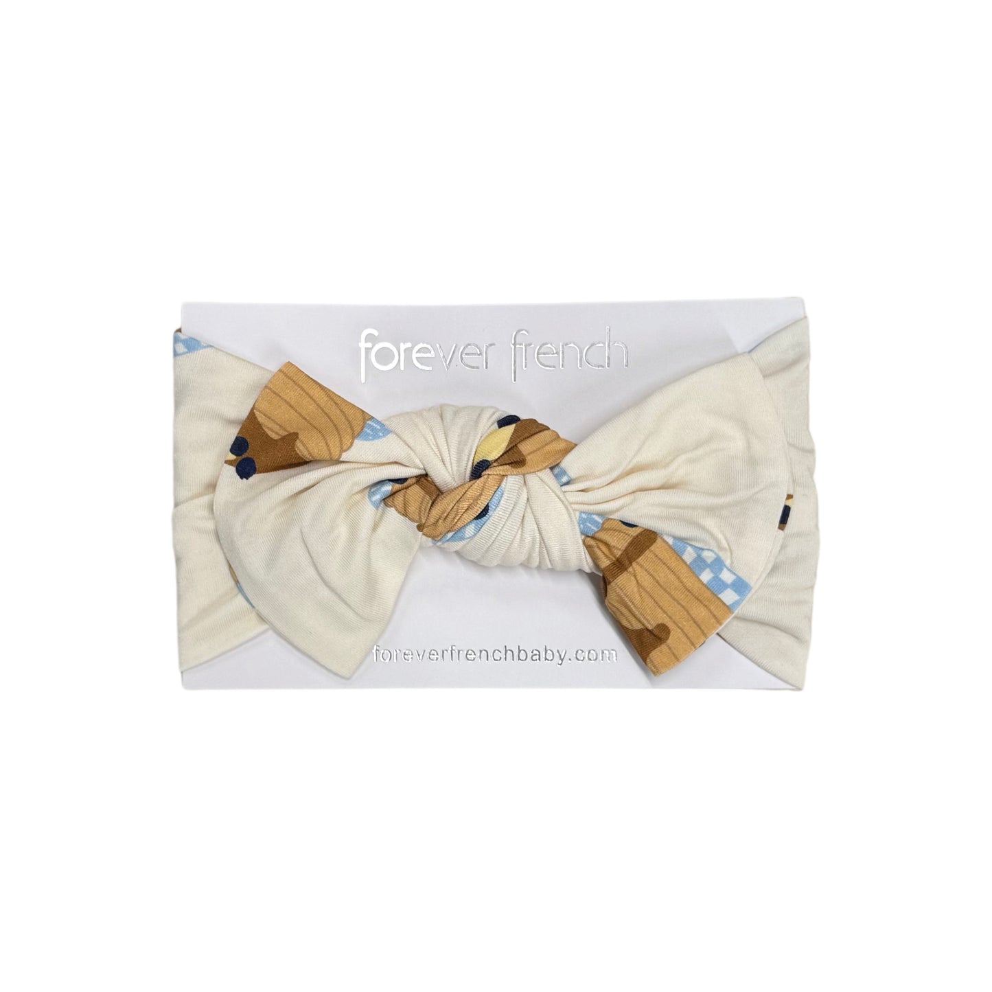 The Bamboo Head Wrap | Sunday Stack by forever french baby is a cream-colored baby headband with a large knot and brown and blue patterned accents, displayed on a white card labeled "forever french baby.