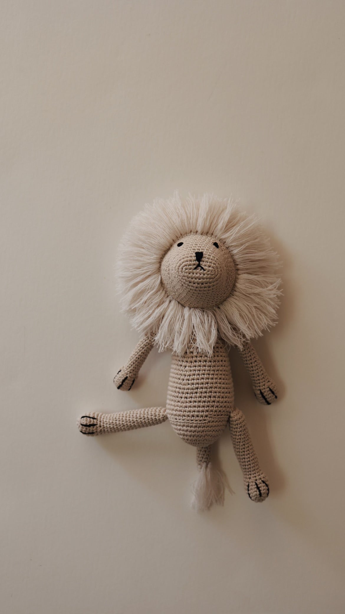 Image of "Lennon the Lion," a handcrafted knit doll from Forever French Baby. It features a majestic mane, small black eyes, and a simple embroidered nose and mouth. The beige stuffed lion exhibits textured limbs and body made from intricate crochet stitches, set against a plain light background.