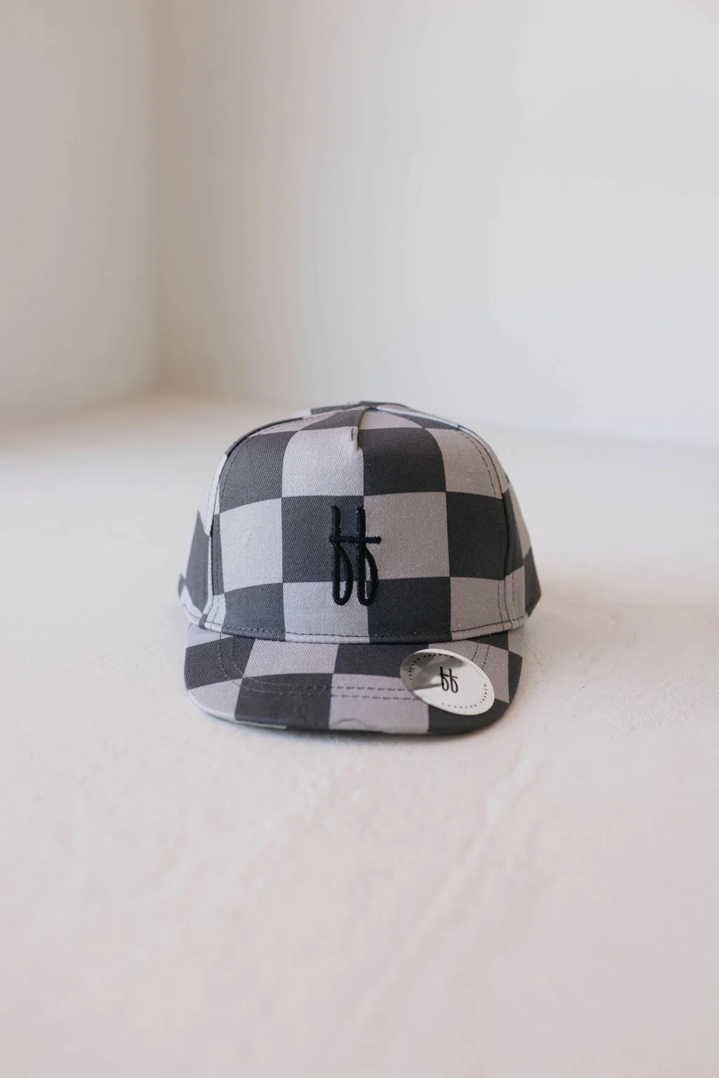 A black and gray plaid cap with a small "bb" logo on the front, placed on a light, neutral surface.