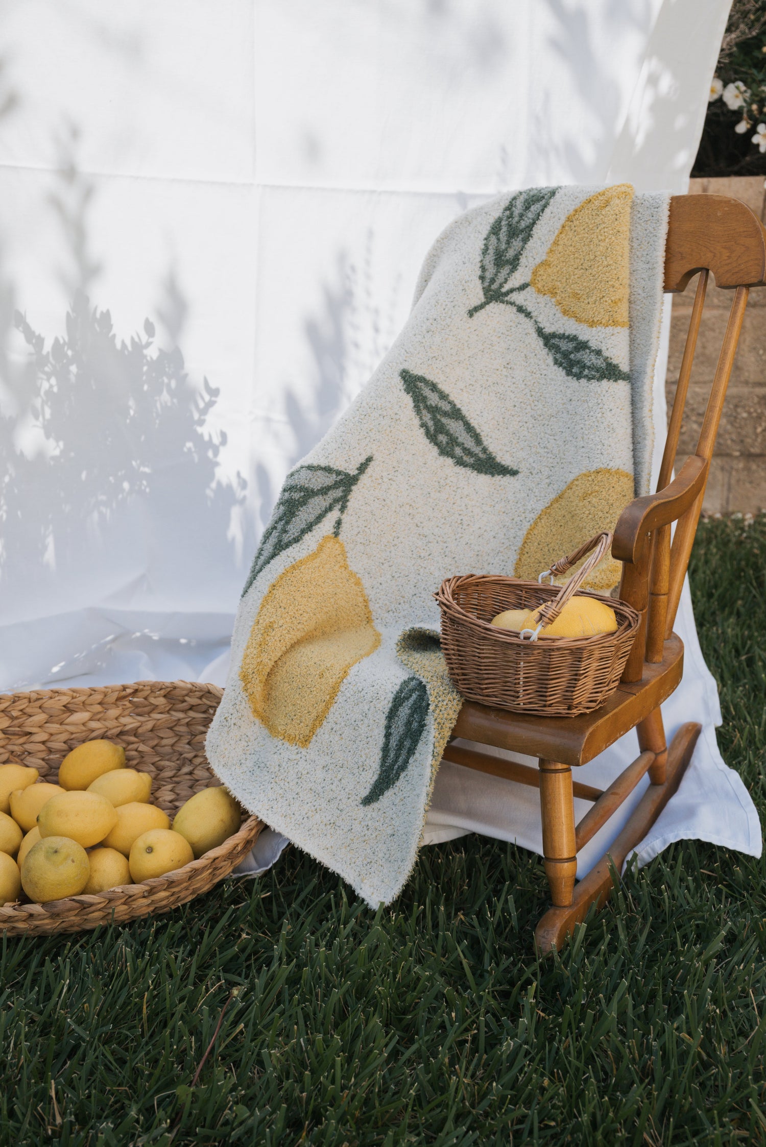 Flat lay of lemon-themed baby and children’s clothing, a bow, and a blanket with lemon designs, all arranged on green grass with several fresh lemons scattered around.