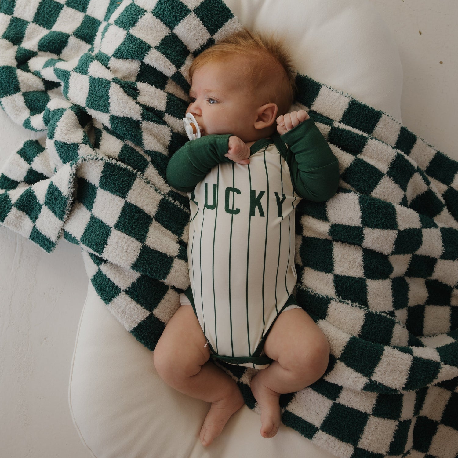 A dark green sweatshirt with the word "LUCKY" in white letters is laid flat next to a black and white checkerboard-patterned knit item on a light background.