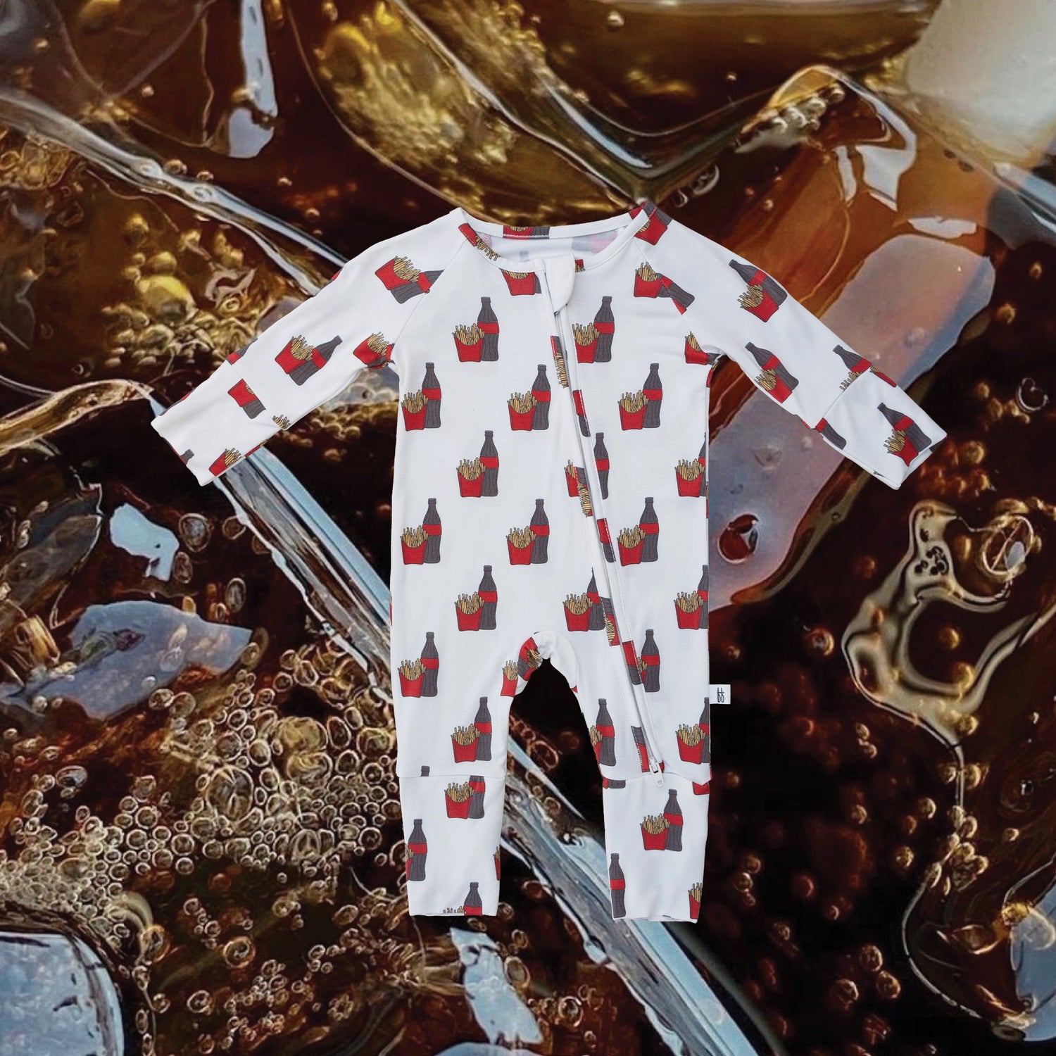 A white baby onesie with a red French fries print is displayed against a close-up background of ice cubes in a dark fizzy drink.