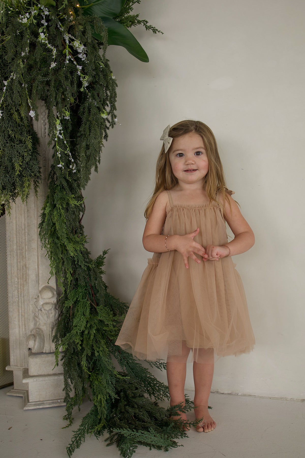 A young girl wearing a beige tulle Tutu Dress | Teddy with a matching hair bow.