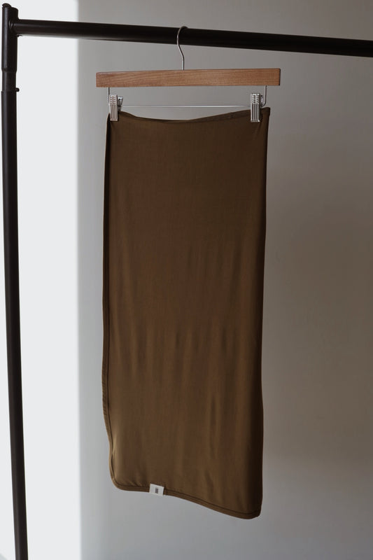 A Bamboo Swaddle in Olive Green from forever french baby hangs neatly on a wooden hanger from a black metal rack against a neutral wall.