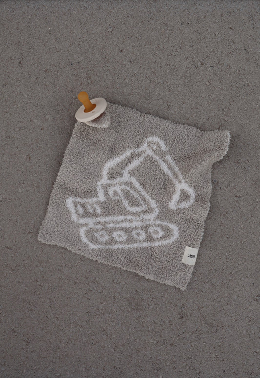 The Lovey | Excavator from forever french baby is a plush gray microfiber lovey with a white excavator outline and an attached brown pacifier, shown on a textured gray surface.