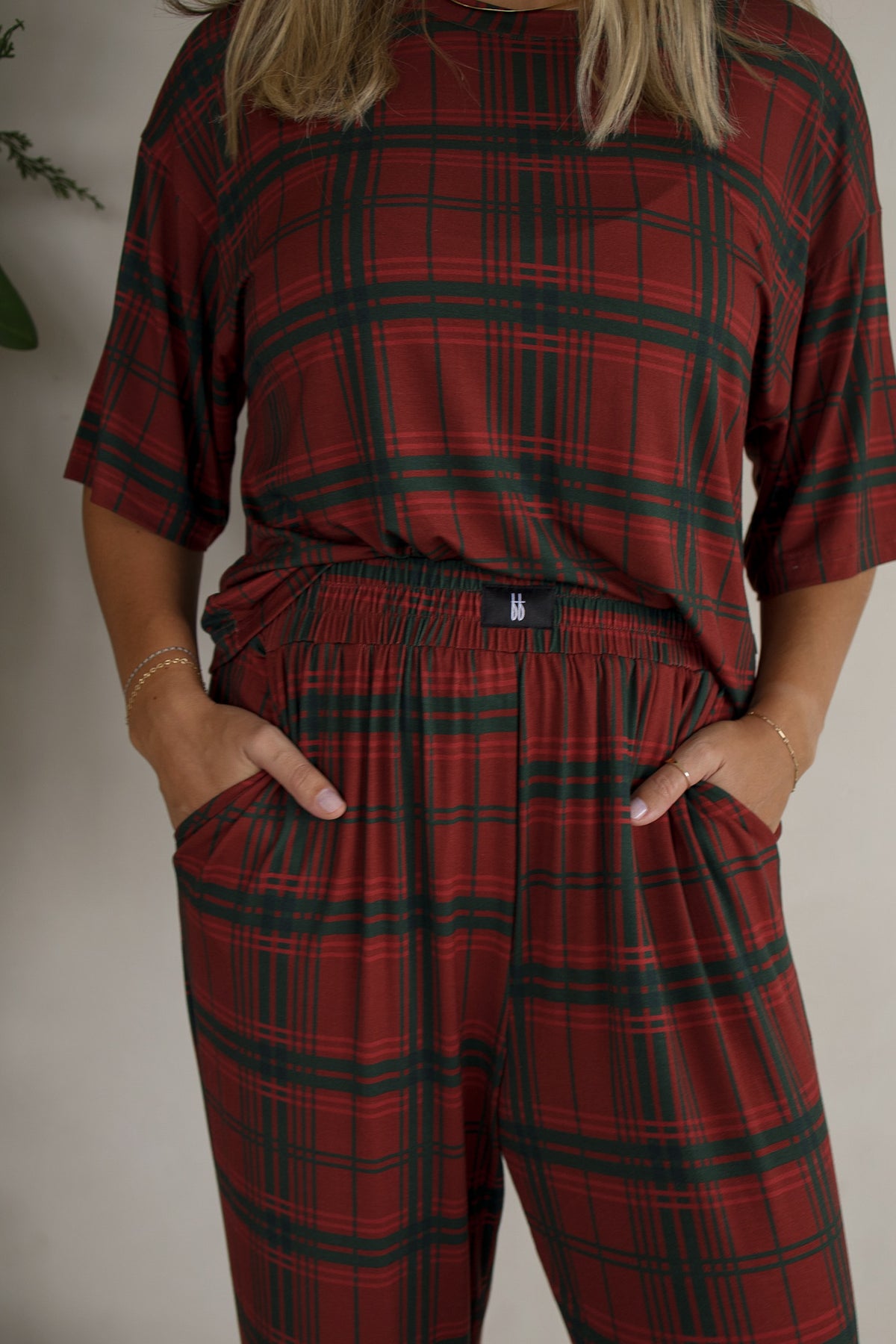 A person wearing a Women’s Boxy Tee Lounge Set | Christmas Plaid featuring a red and dark green plaid lounge top and matching drawstring pants.
