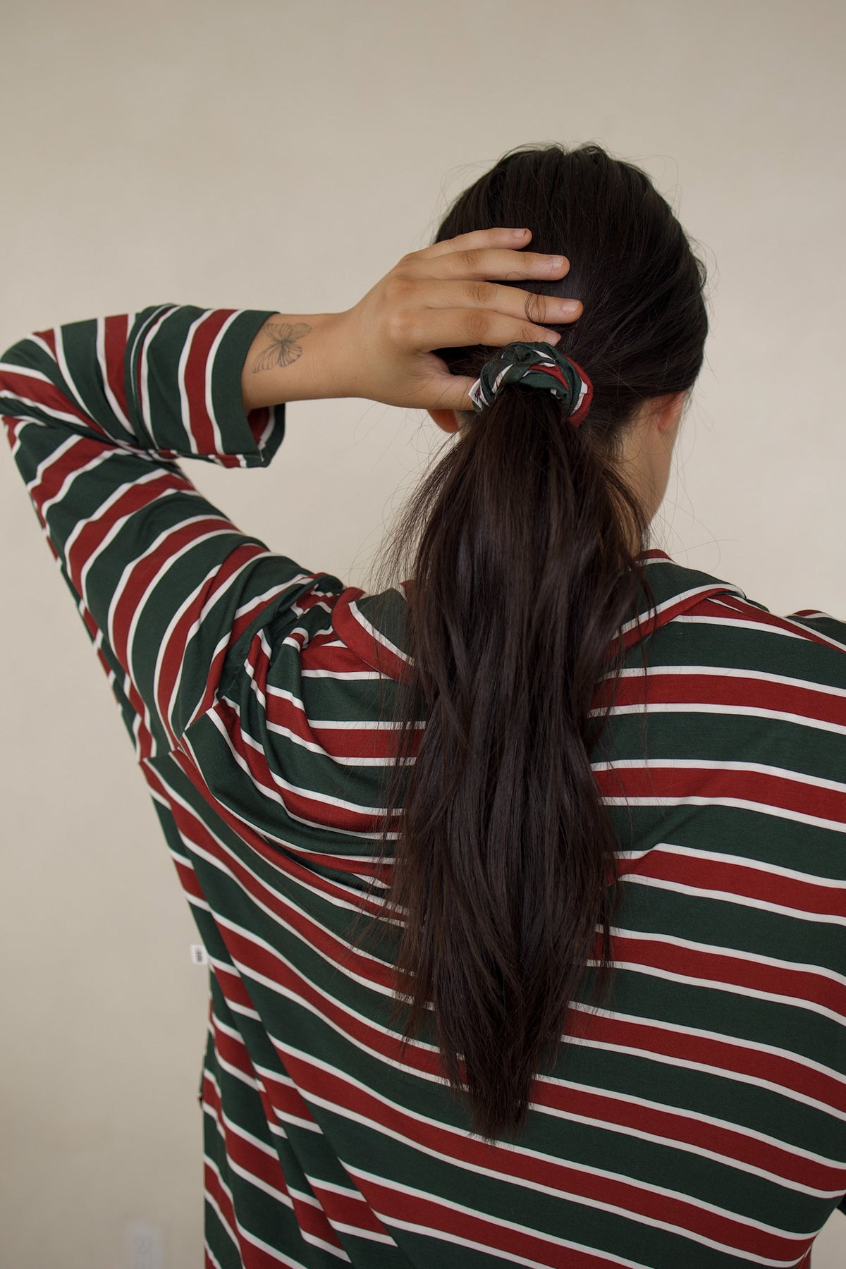A person with dark hair in a ponytail secured by a Forever French Baby Scrunchie | Holiday Stripe in green, red, and white.