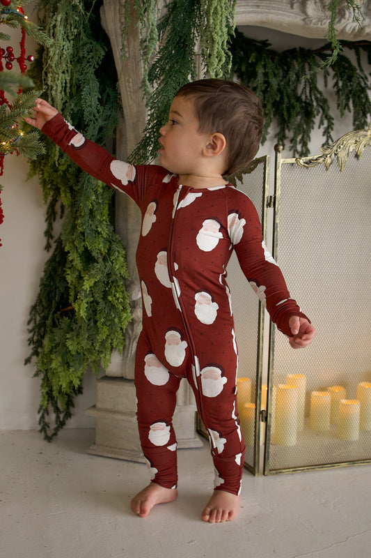 A toddler wearing Bamboo Zip Pajamas | Vintage Santa reaches toward a decorated Christmas tree.