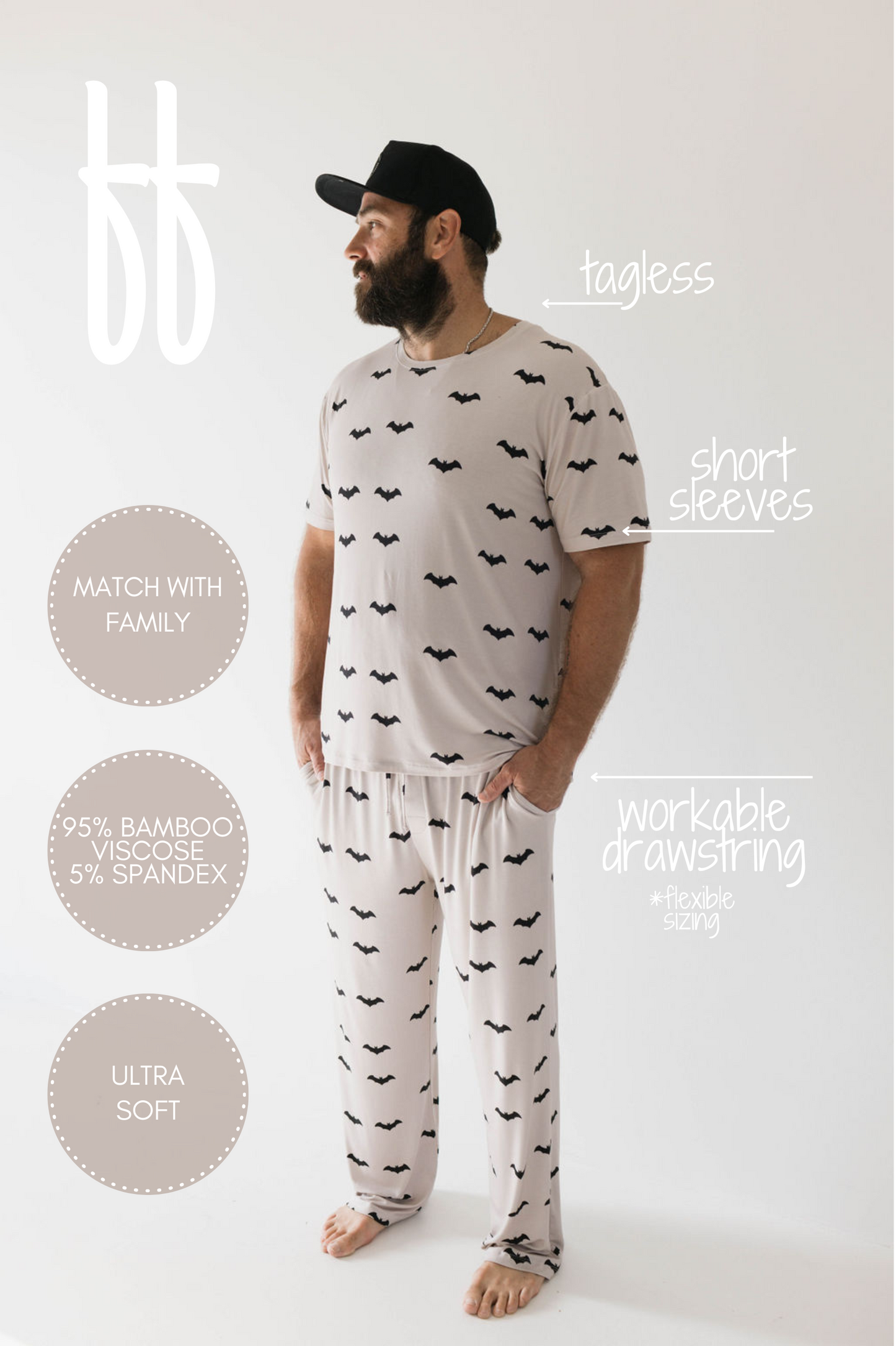 A man with a beard and a black cap is wearing the Adult Bamboo Short Sleeve Pajamas from forever french baby, featuring a cream color adorned with a black bat pattern. These hypoallergenic pajamas boast short sleeves, are tagless, offer an ultra-soft texture, and come with a workable drawstring for adjustable sizing. The hypoallergenic properties of these pajamas are prominently highlighted in the image text.