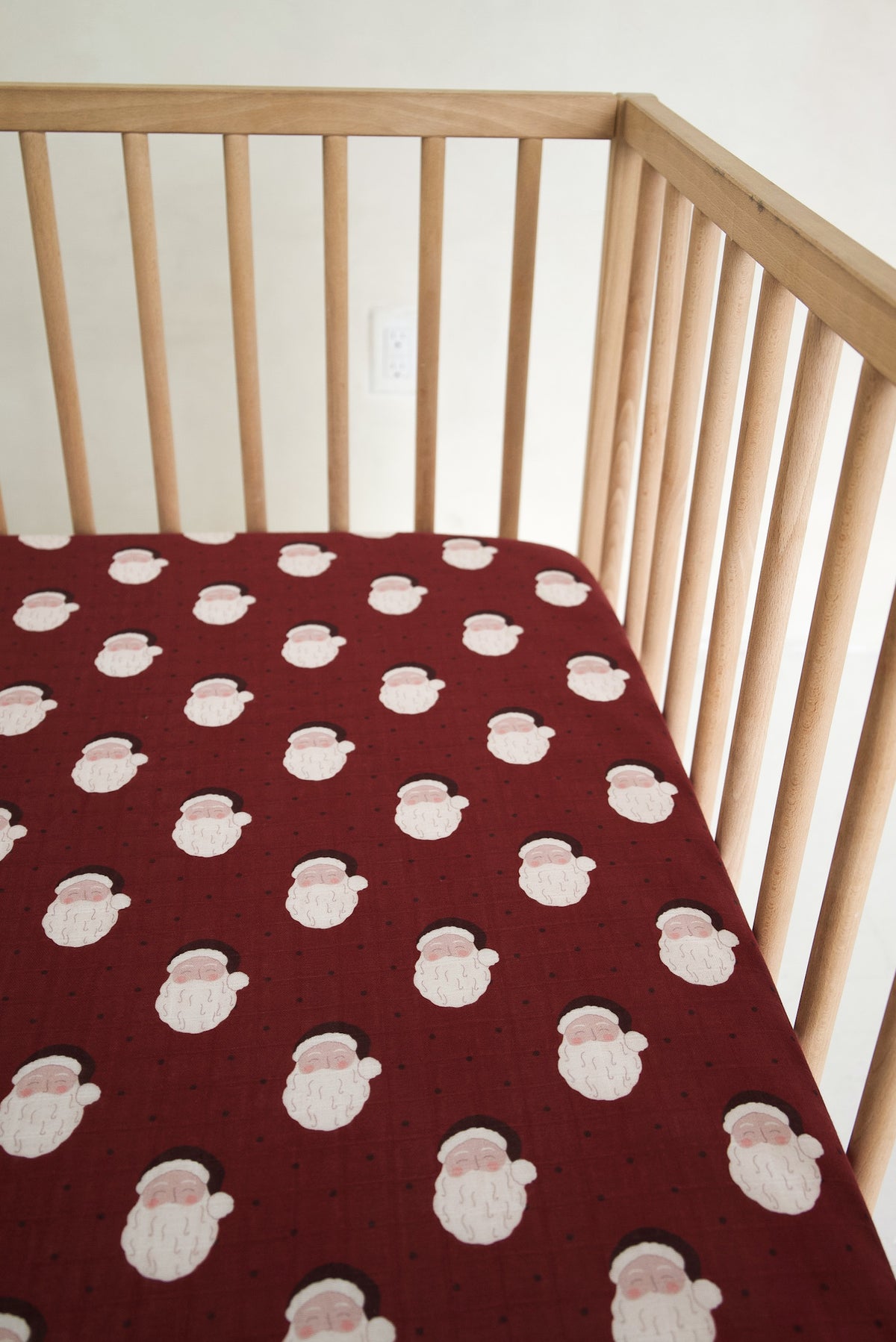 Muslin Crib Sheet | Vintage Santa featuring a repeating pattern of Santa Claus faces on a dark red background.