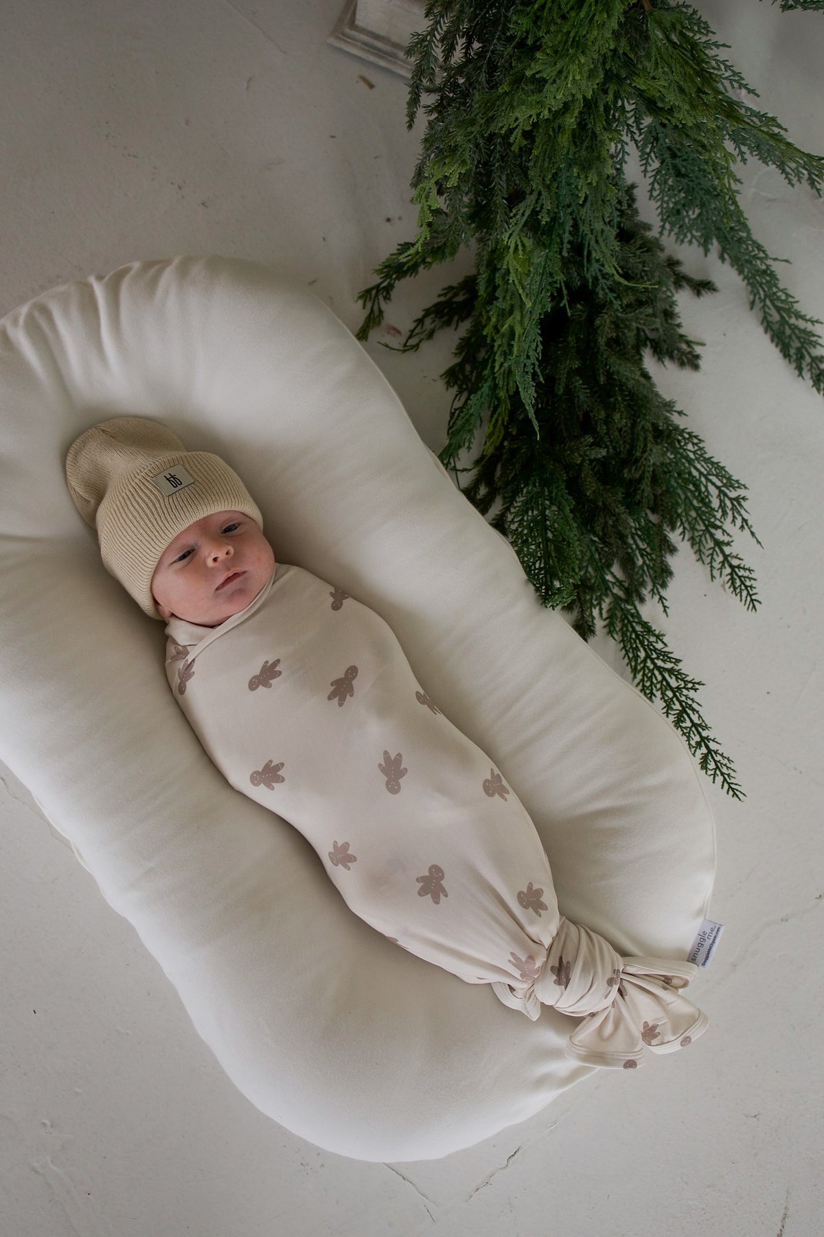 A newborn baby in a tan beanie swaddled in a forever french baby Bamboo Swaddle | Gingersnap, resting in a white baby lounger.