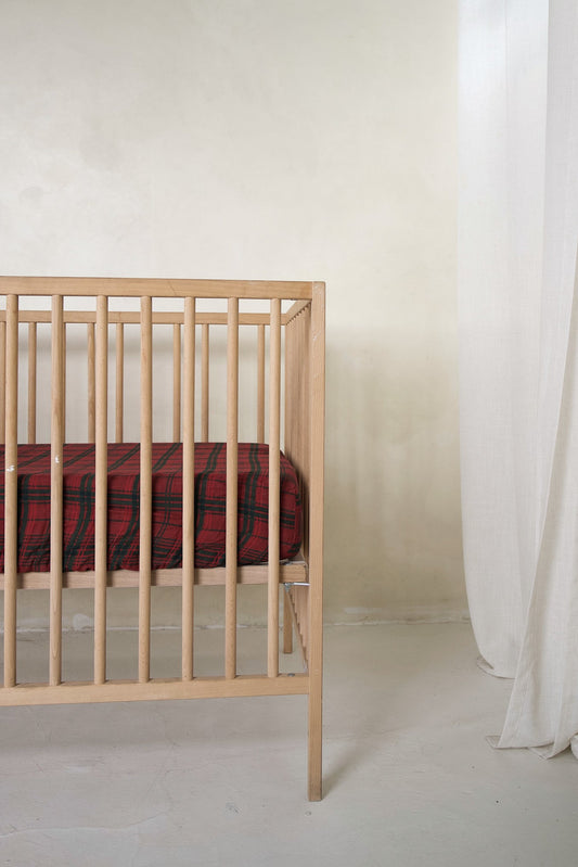 A wooden crib with a red and black Muslin Crib Sheet | Christmas Plaid by forever french baby.