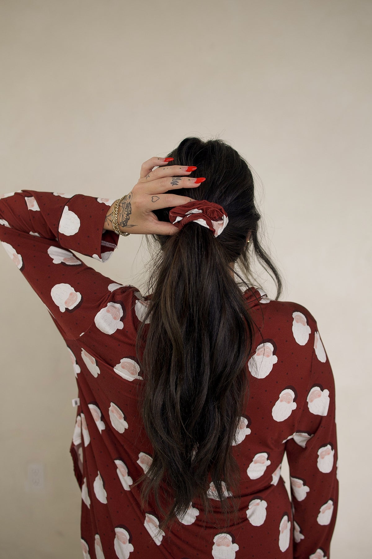 A person wears a Forever French Baby Scrunchie | Vintage Santa in burgundy with a repeating vintage Santa print, matching their long-sleeved shirt.