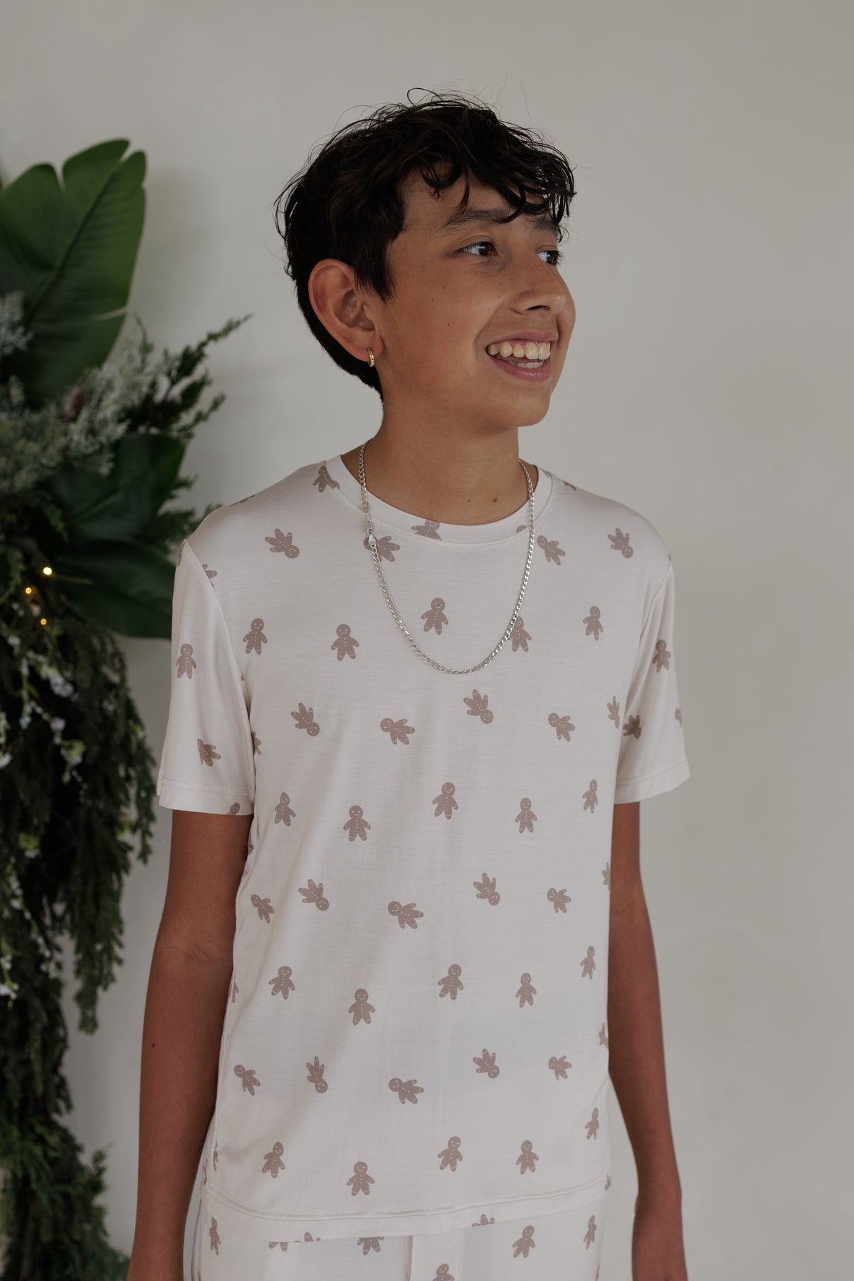 A boy wearing a short-sleeved Youth Straight Leg Bamboo Pajamas | Gingersnap top with an all-over gingerbread man print.