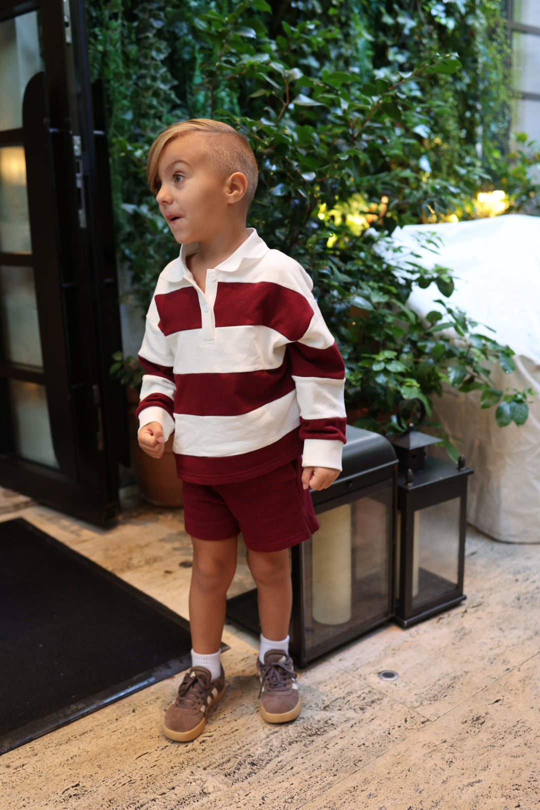A young child wears a long-sleeved, 100% cotton white-and-burgundy striped Child Rugby Sweatshirt | Deep Cranberry with matching burgundy shorts.