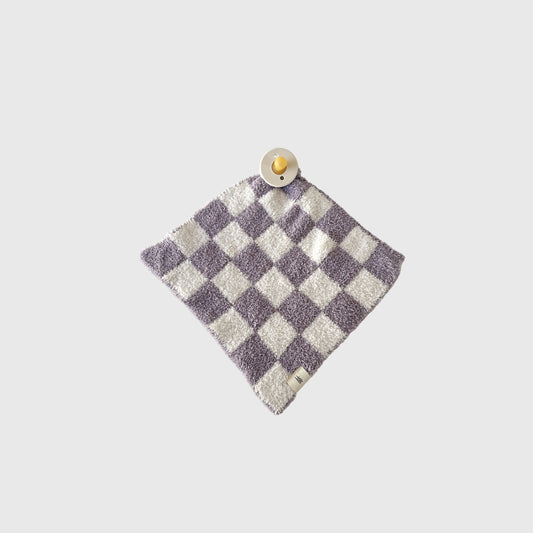The Lovey | Grape Soda by forever french baby, a purple and white checkered microfiber blanket, is laid flat on a light gray background with a beige pacifier resting on one corner.