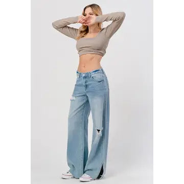 A person stands confidently in a neutral long-sleeve crop top and High Rise Skater Jeans in Medium Wash from I&M JEAN, INC. They have their hands on their head, wearing white sneakers, set against a plain white background.