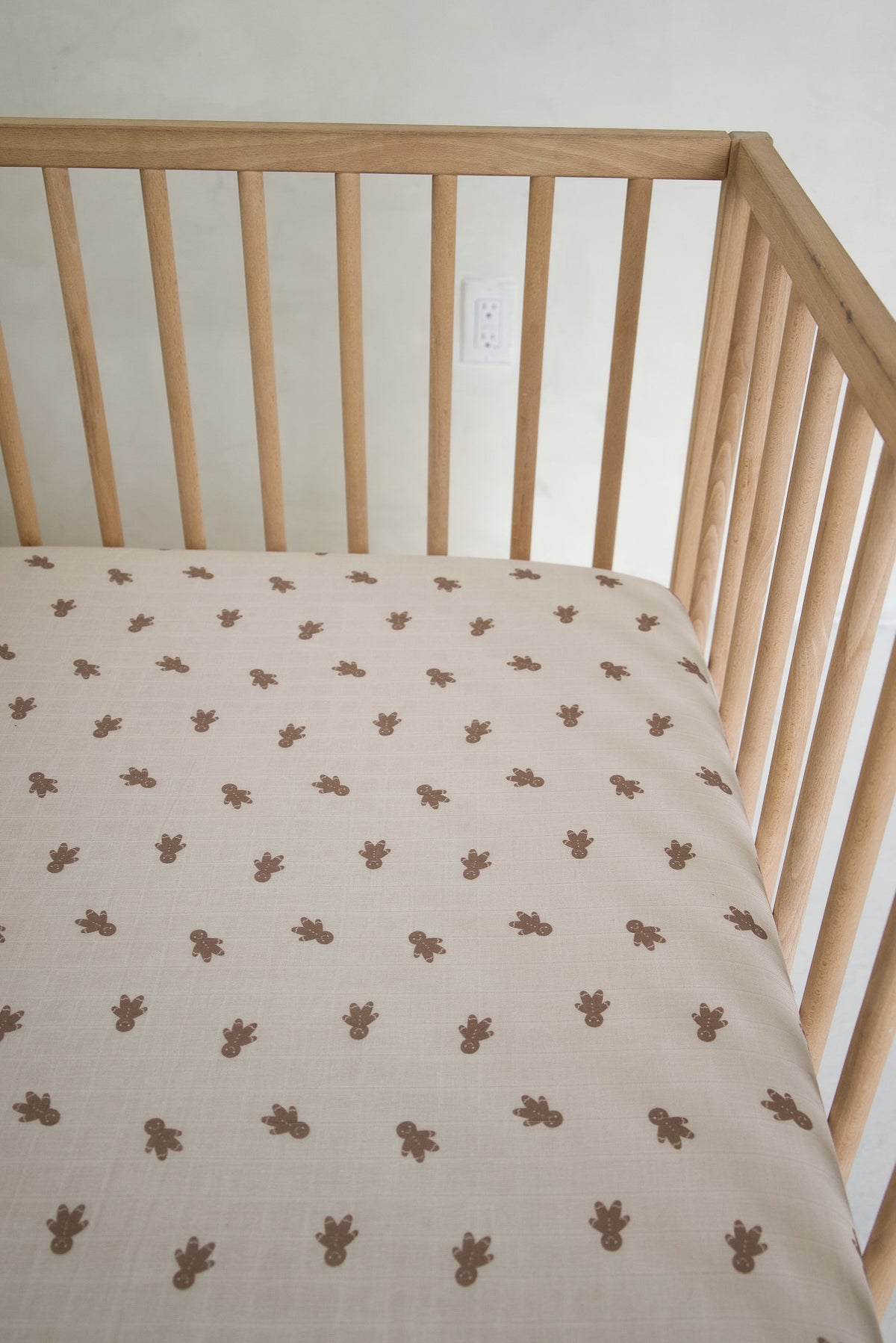 A forever french baby Muslin Crib Sheet | Gingersnap featuring a repeating pattern of brown gingerbread men inside a wooden crib.