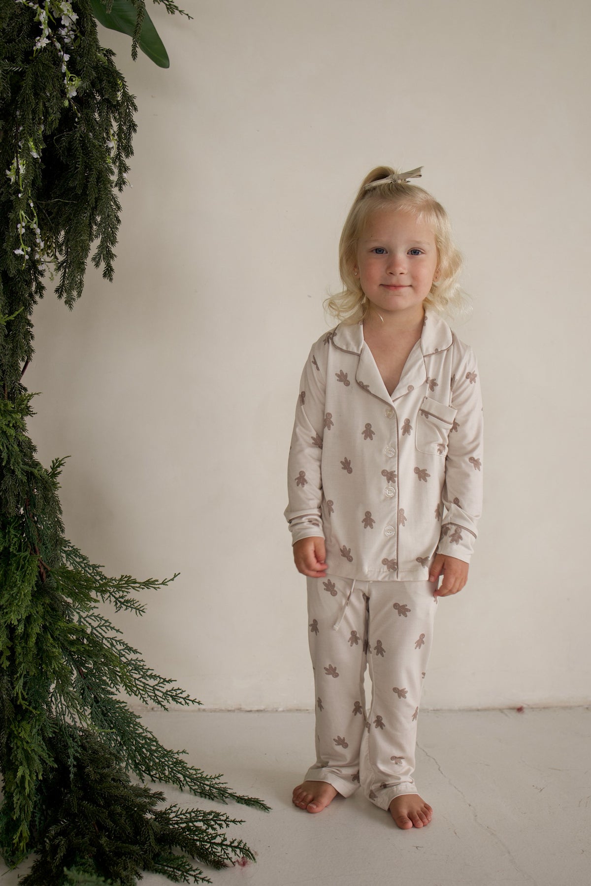A young girl wearing a Girl’s Bamboo Button Up Lounge Set | Gingersnap featuring a gingerbread man print.