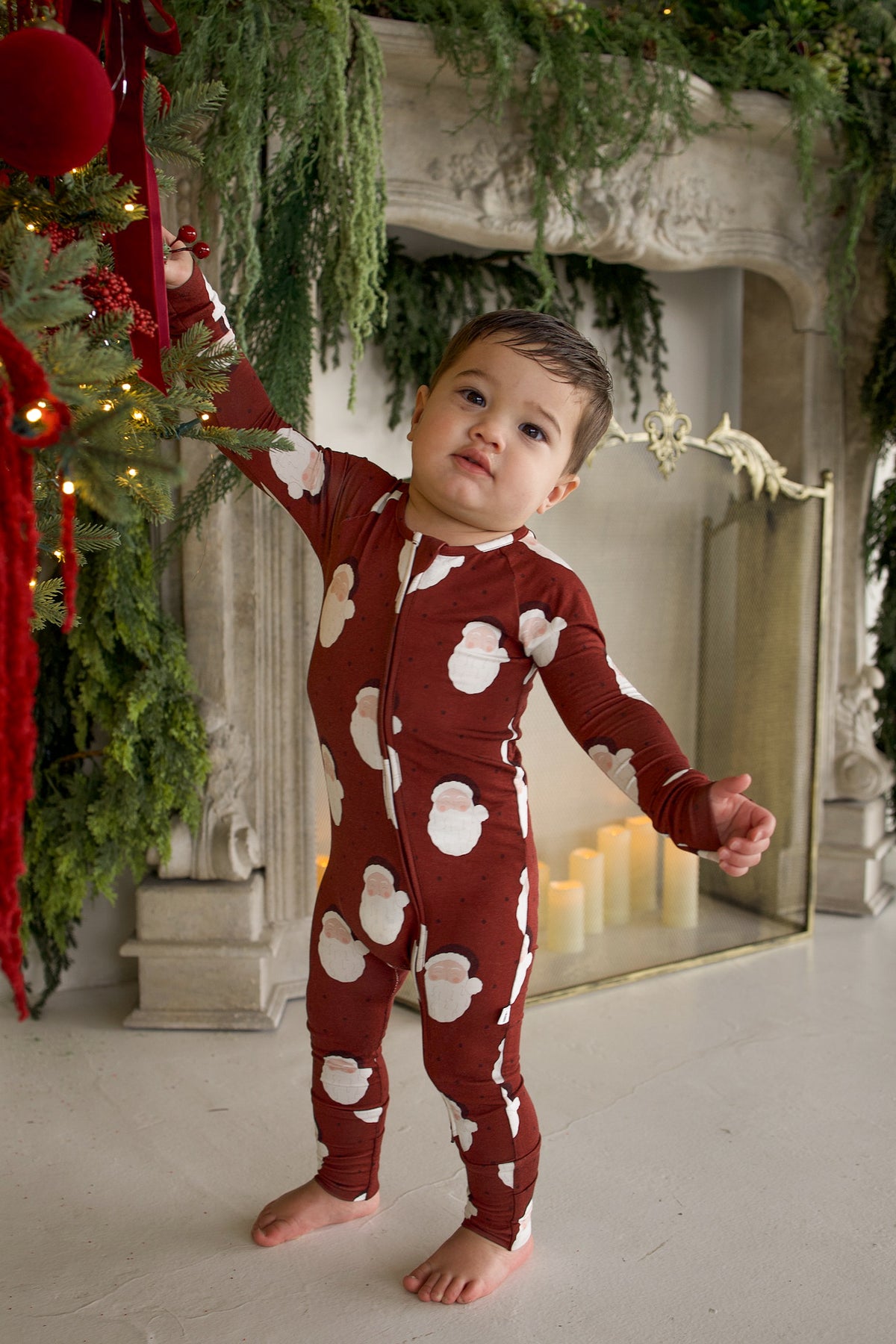 A toddler wearing Bamboo Zip Pajamas | Vintage Santa stands by a Christmas tree.