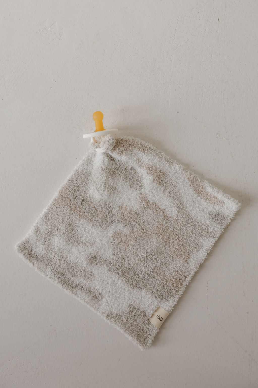 The forever french baby Lovey | Camo 2.0 is a soft, square microfiber plush with a neutral camo pattern and an attached pacifier, perfect for comfort and security.
