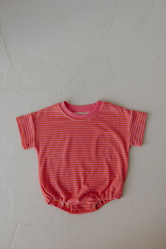 The forever french baby Terry T-Shirt Romper | Strawberry features pink and orange stripes, pink neck trim, and short sleeves. Designed for easy diaper changes, it's laid flat on a light textured surface.