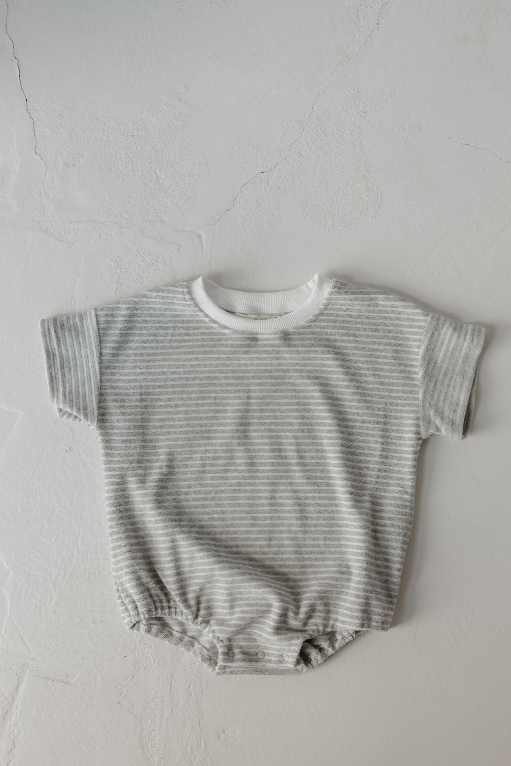 The Terry T-Shirt Romper | Grey Stripe by forever french baby features short sleeves, light gray and white stripes, and convenient bottom buttons—ideal for easy diaper changes during family moments.
