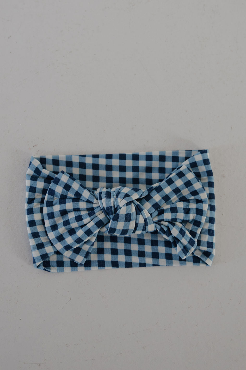 The forever french baby Bamboo Head Wrap | Blue Gingham features an adjustable design with a large central bow in a classic blue and white gingham pattern, shown on a plain light surface.