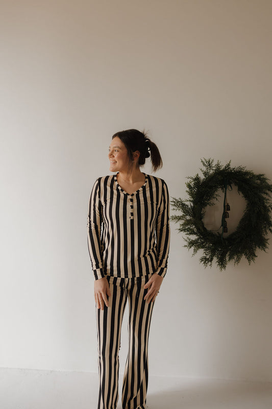 A woman wearing the forever french baby Women's Long Sleeve Bamboo Pajama in Midnight Stripe stands indoors beside a green wreath on a light wall, looking to her left.