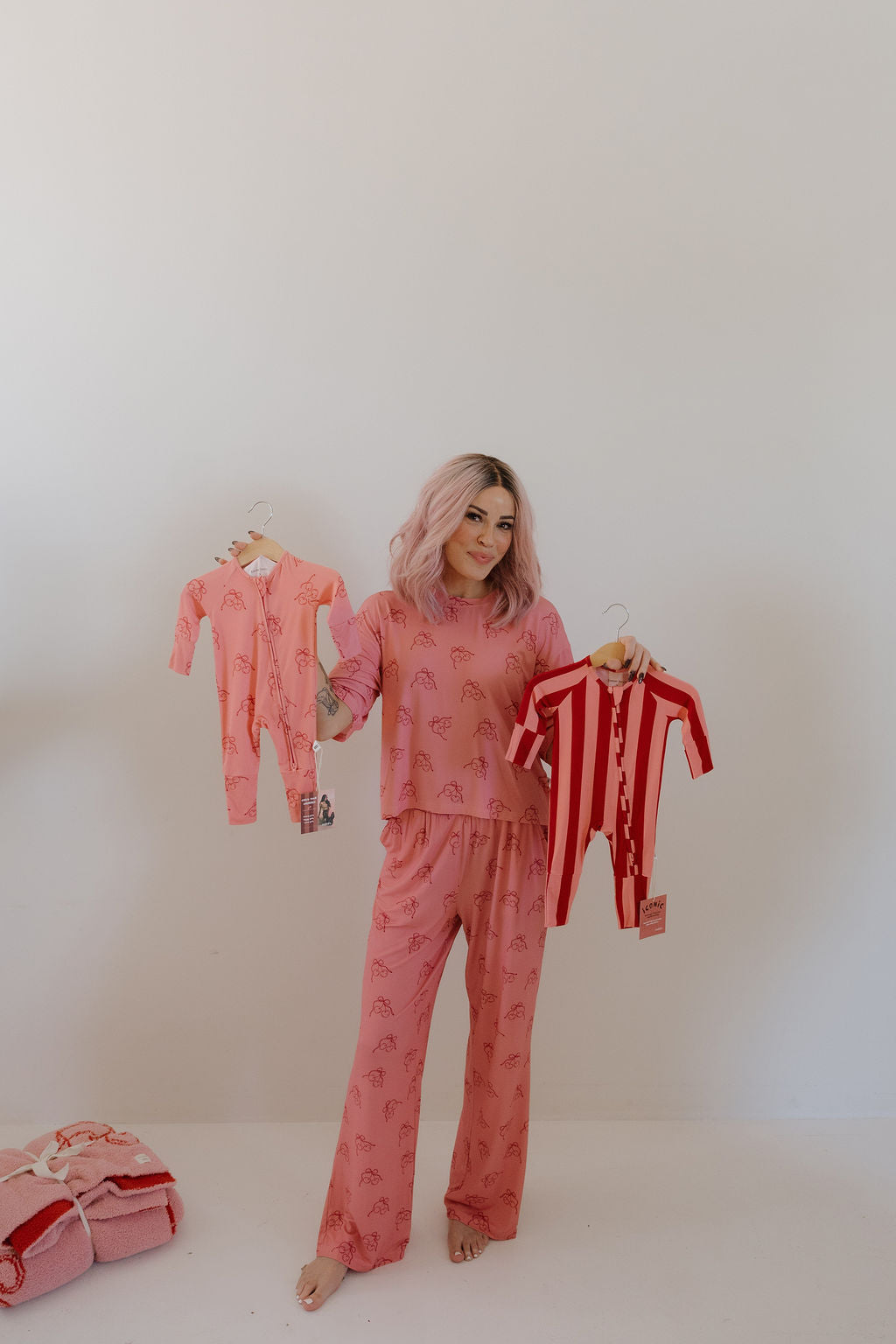 A woman with pink hair in pink pajamas stands barefoot in a minimalist room, showcasing Minty Cherries' Women's Boxy Tee Lounge Set | Iconic Cherry with a pink blanket on the floor.